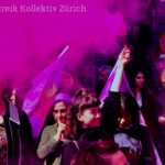 Foto von der 1. Mai Demonstration, Junge Frau hält Rauchstab mit violettem Rauch in die Höhe, ringsherum weitere Demonstrantinnen