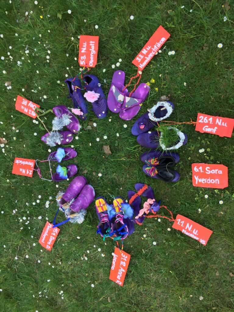 Ein Foto von 9 paar violettgeförbte Schuhe jeweils mit einem Schildchen mit jeweils einem Namen und Datum der 9 Frauen, die seit Anfang 2020 bis jetzt (25.4.) ermordet wurden in der Schweiz