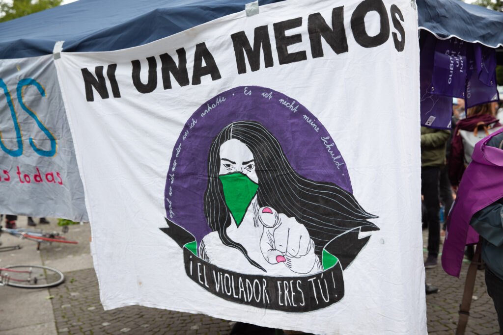 Transparent: "NI UNA MENOS", darunter gemalt eine langhaarige Person, darunter geschrieben "!El ViOLADOR ERES TU!"