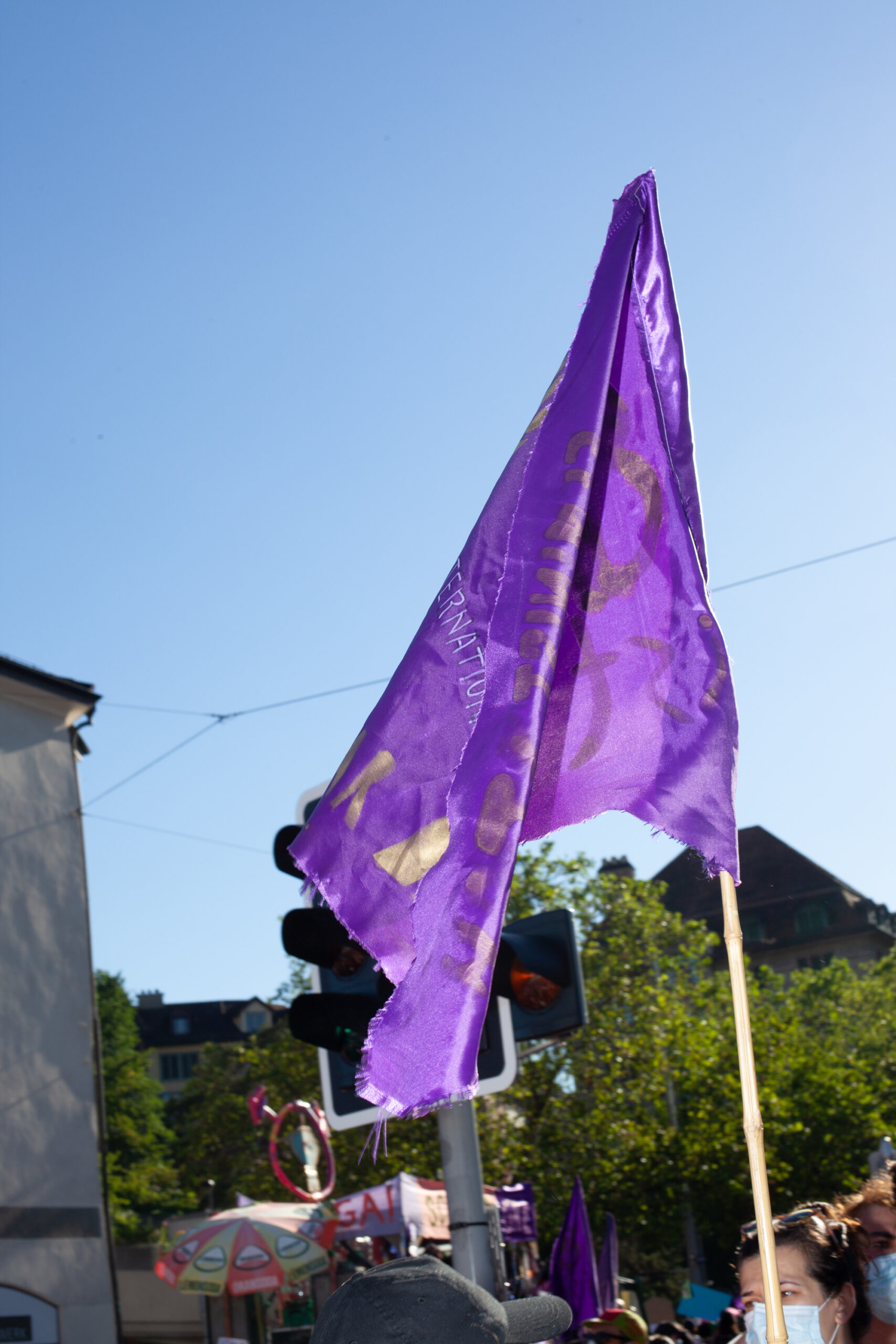 Ein Foto einer violettn Fahne die an eine Stange in den Himmel gehalten wird. sie ist mit weiss und gold beschriftet, aber es ist nicht lesbar was steht weil die Fahne gerade Falten im Wind schlägt
