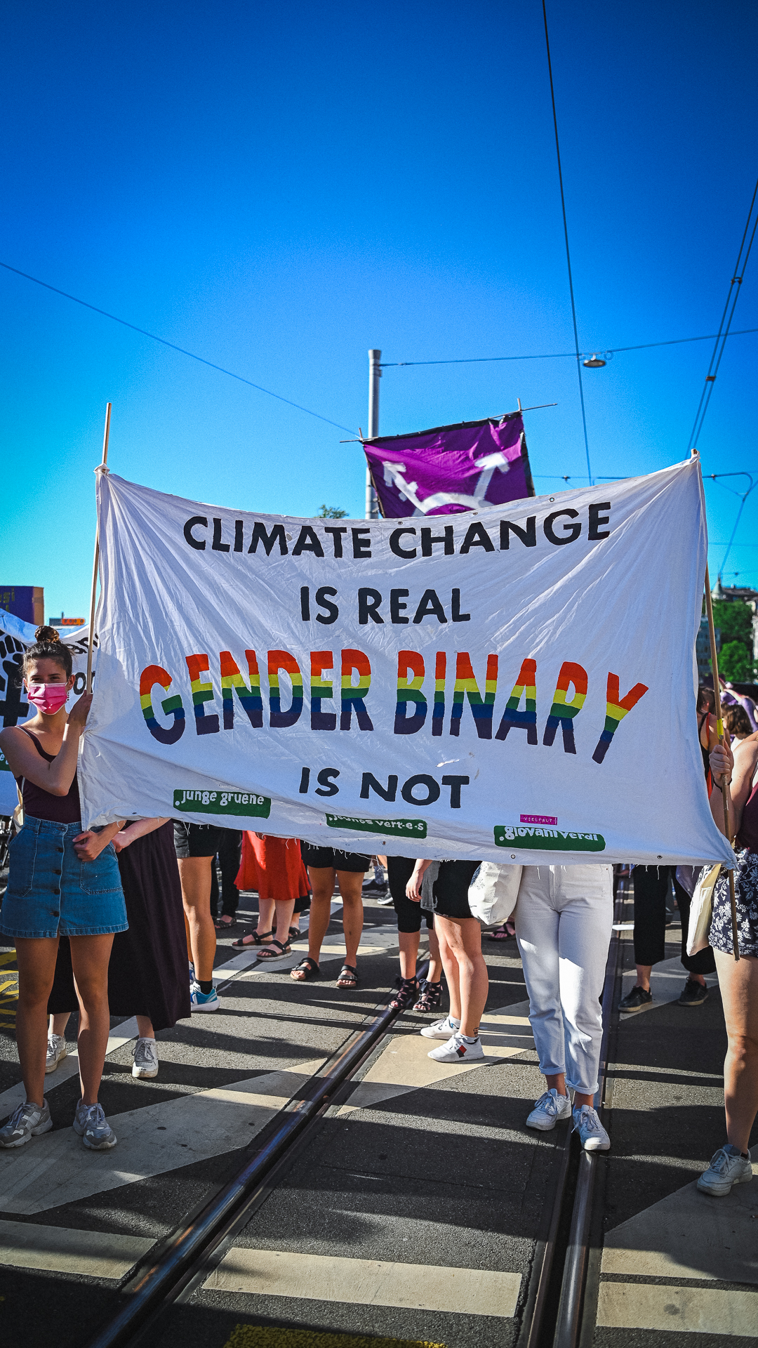 Ein Transparent in der Demo auf dem Limmatquai. Darauf steht: "Climat Change is real Gender Binary is not" und das logo der jungen grünen. "Gender Binary" ist in Regenbogenfarben geschrieben.