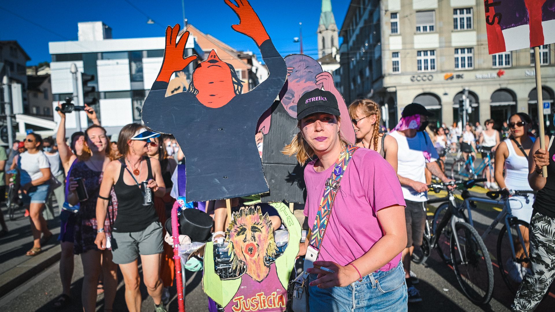Foto von der Demonstration am 14.6. in Zürich, die Klageweiber, aus Pappe gefärtigte Figuren von schreienden und klagenden Frauenfiguren werden von mehreren FLINTA transportiert.